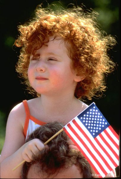 Redhead girl with American flag sitting on dad's shoulders 
